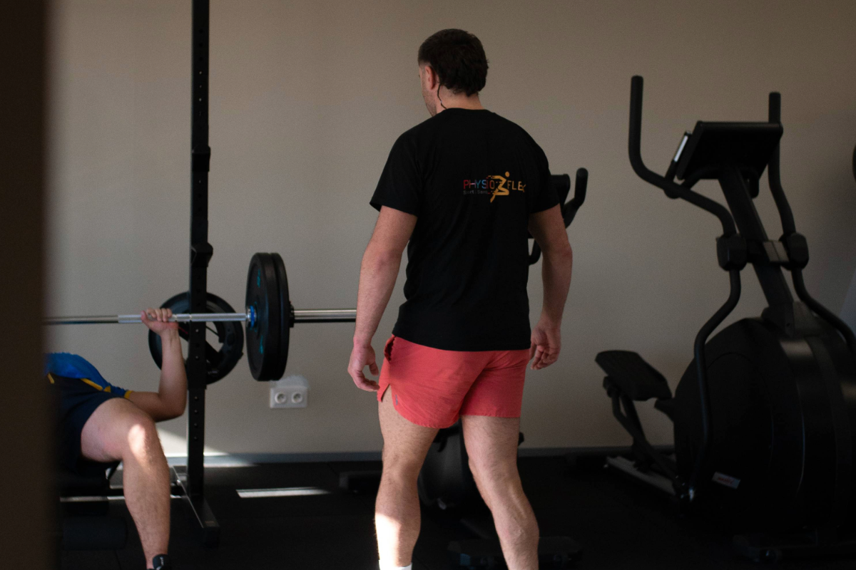 Prof de sport s'approche d'un élève faisant du développé couché, dans une salle de sport