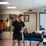 Photographie d'un cabinet de kinésithérapie, un kiné se dirige vers son patient allongé