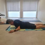 Deux personnes effectuant du gainage sur un tapis de yoga au sol dans une pièce