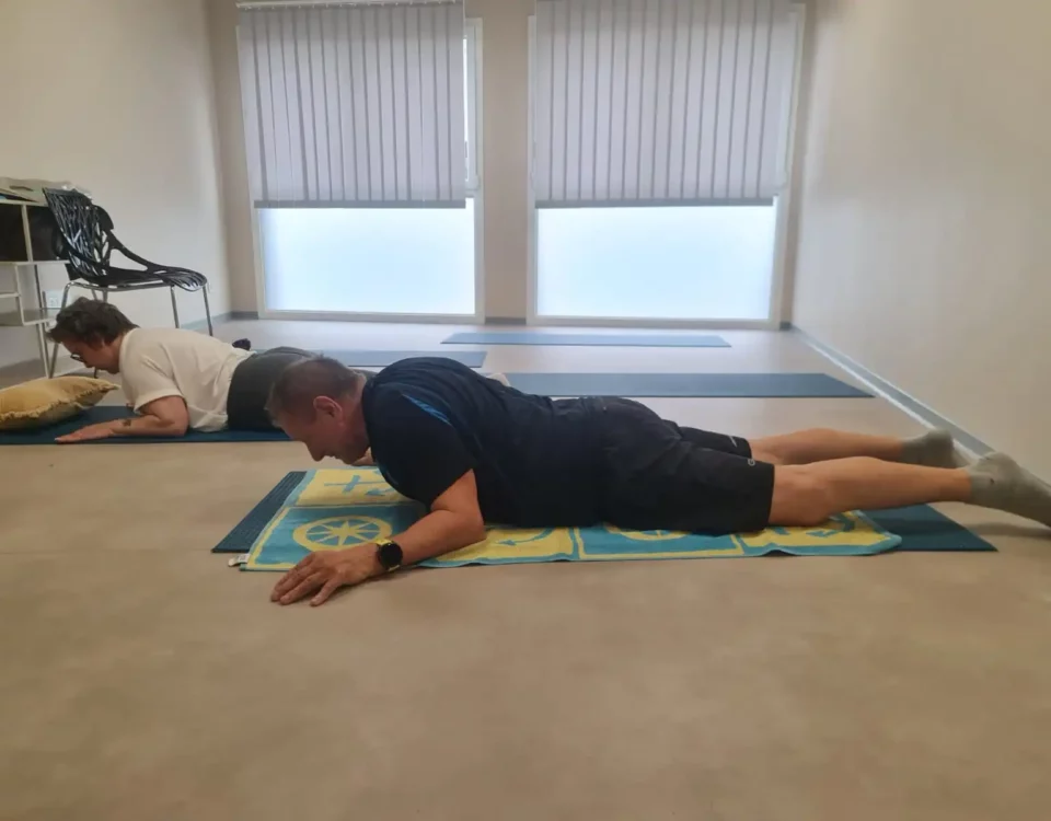 Deux personnes effectuant du gainage sur un tapis de yoga au sol dans une pièce