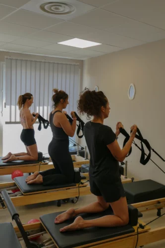 Trois personnes faisant une séance de sport sur des machines de pilates sur reformer